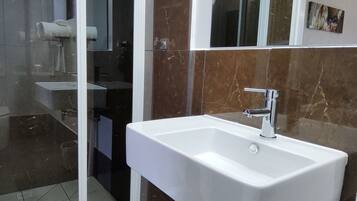 Un baño con un lavamanos blanco, un espejo y una cabina de ducha de vidrio.