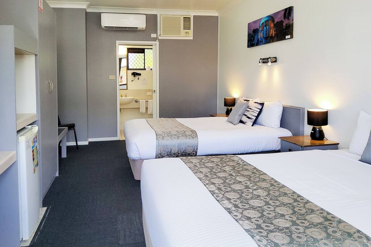 A hotel room with two beds, a bathroom, and a hallway leading to another room.