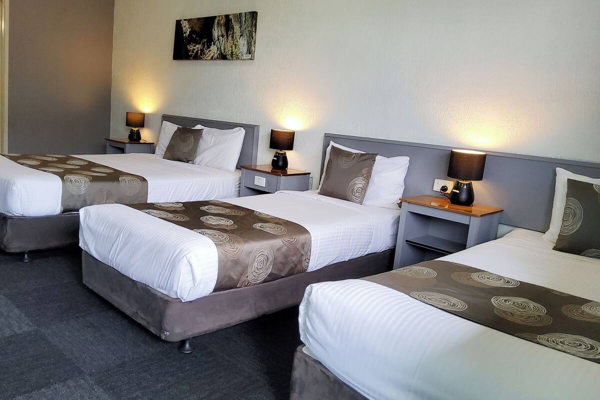 A hotel room with three beds, each with a headboard, bedside tables, and lamps.