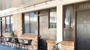 A building with a brick facade, a black door with a number, and outdoor seating with chairs and tables. - Archer Park Motel (Rockhampton)