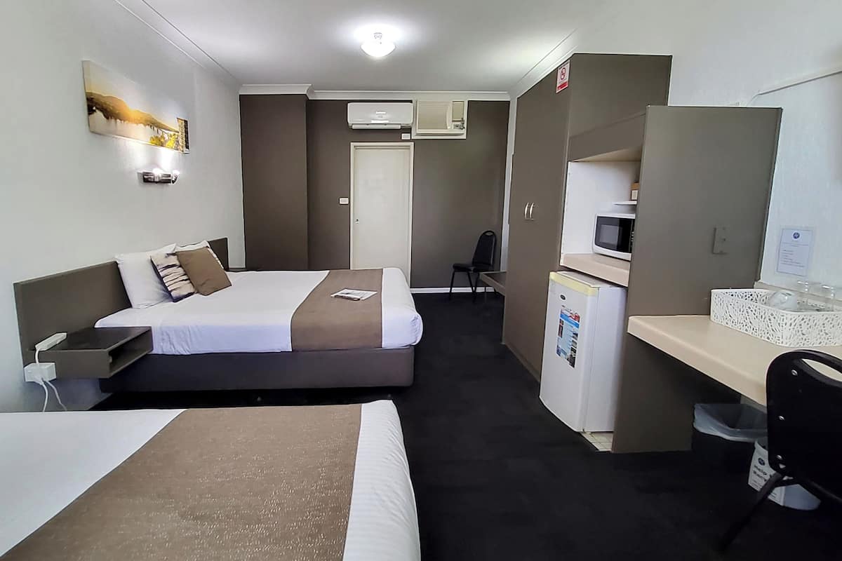 A hotel room with two beds, a desk, a chair, a microwave, and an air conditioning unit.