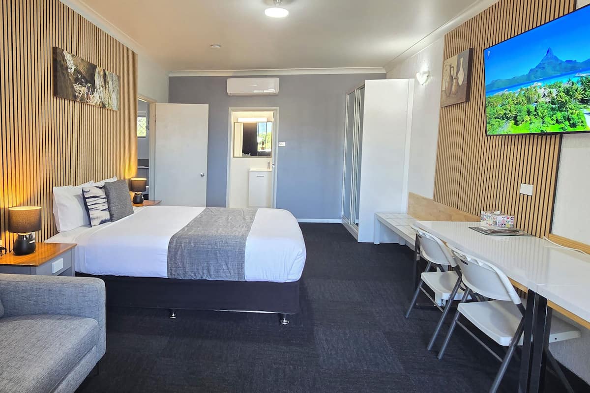 A hotel room with a bed, a desk, a chair, a TV, and a wooden wall panel.