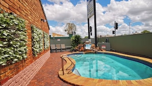 A swimming pool with a brick wall and greenery on one side, a 'No Entry' sign, and a 'No Smoking' sign in the background. - Archer Park Motel (Rockhampton)