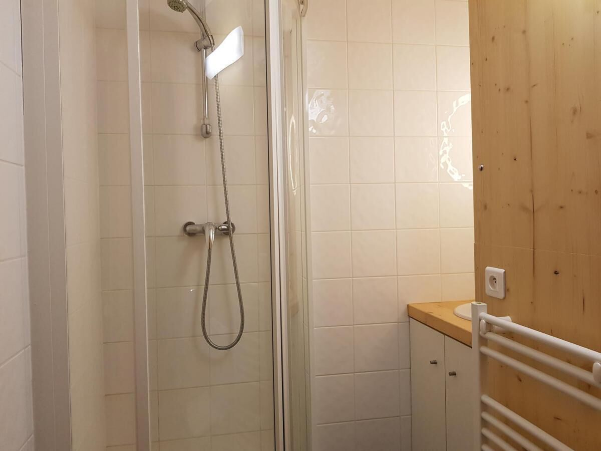 Ducha con puerta de vidrio, panel de pared de madera y suelo con baldosas blancas.