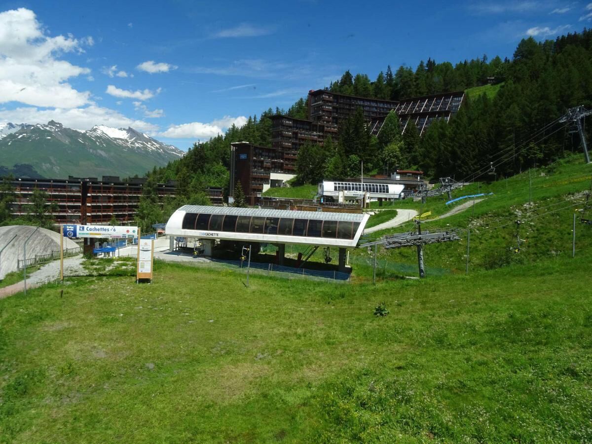 A modern building with a glass facade, surrounded by lush greenery and mountains in the background.