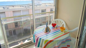 Un balcón con una mesa, una silla y vista al mar y edificios.