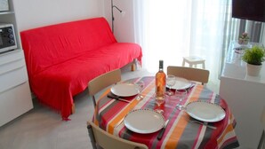 Un comedor con una mesa preparada para cuatro, un sofá rojo, una mesita con una planta en maceta y un cuadro en la pared.