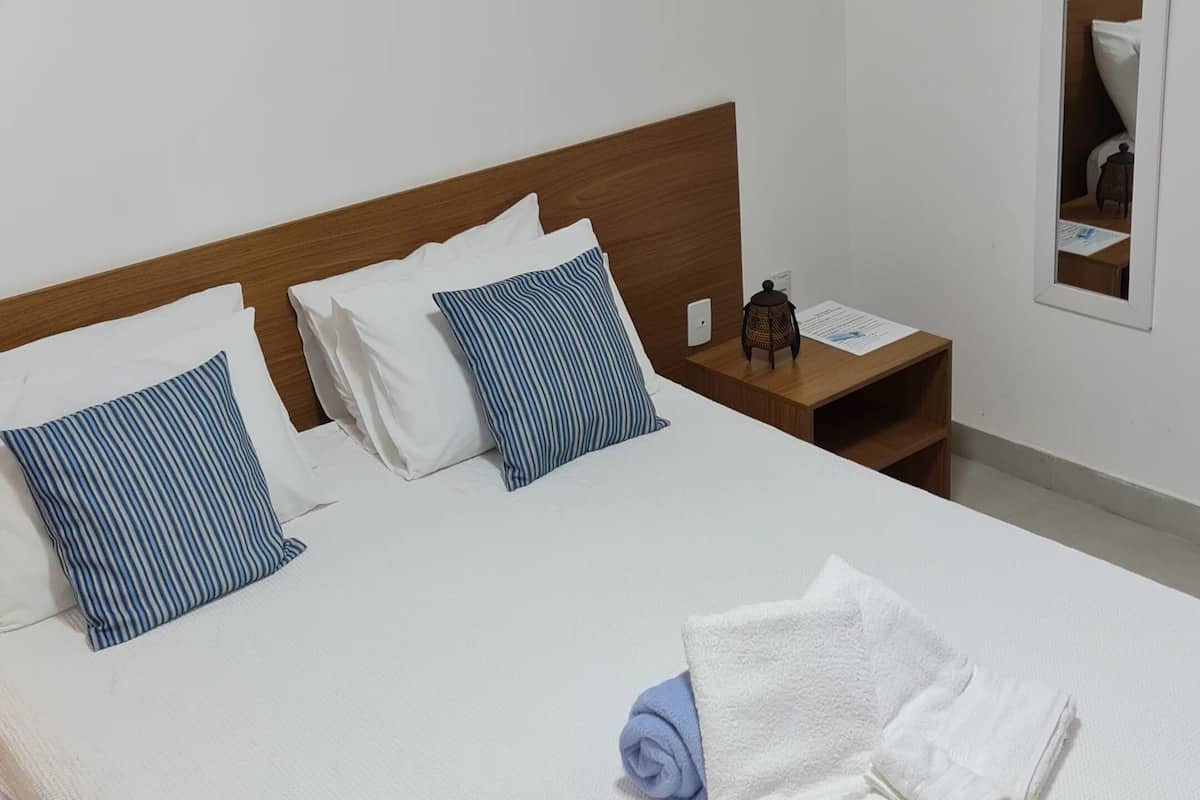 A neatly made bed with white and blue striped pillows, a wooden headboard, and a nightstand with a lantern and papers.