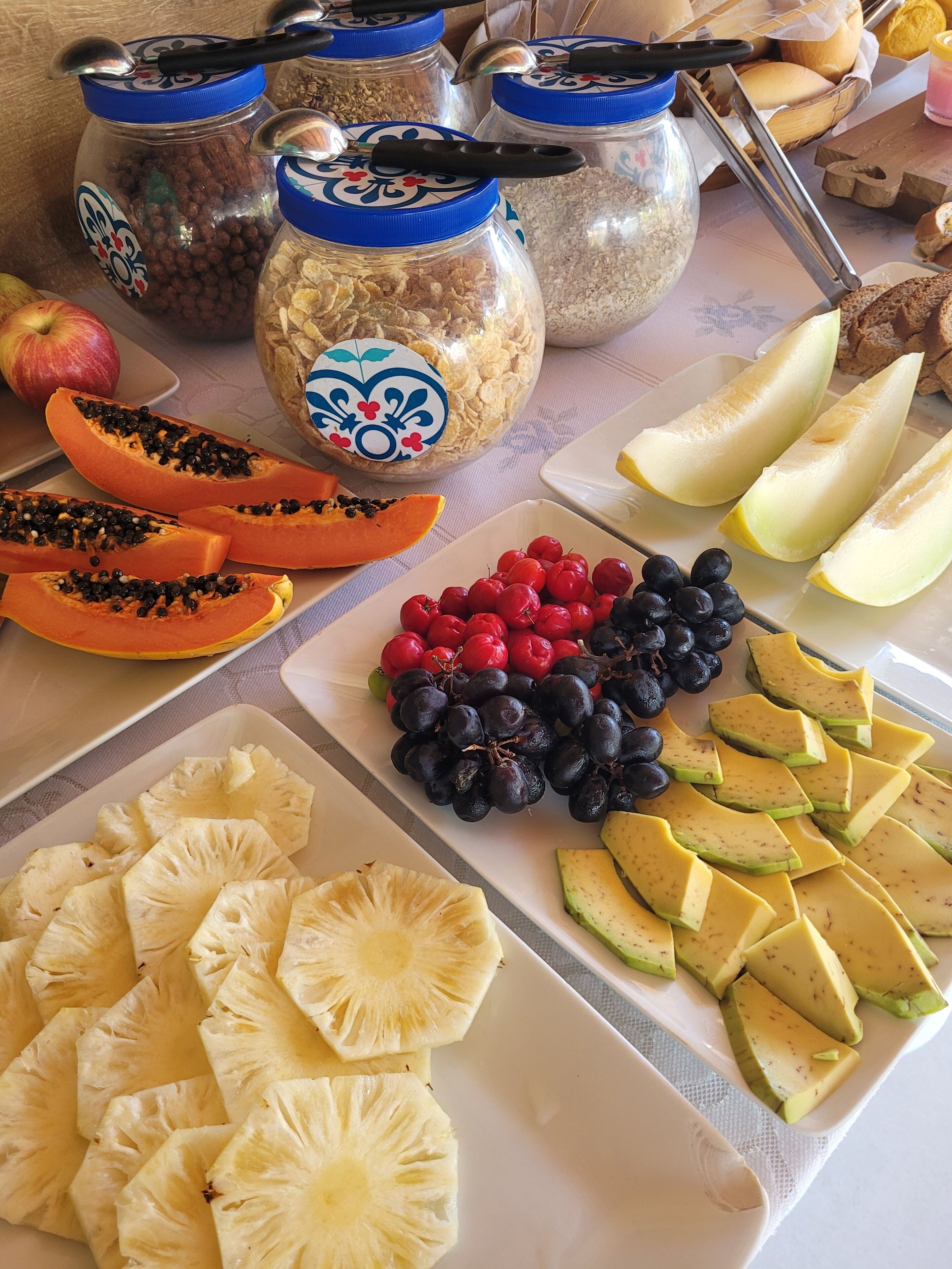 A table with various fruits and snacks, including sliced apples, papaya, grapes, and pineapple.