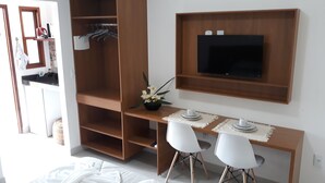 Un dormitorio con una cama, un armario de madera, un escritorio con dos sillas, un televisor y una planta pequeña.