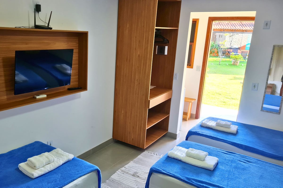 A room with a TV mounted on the wall, wooden shelves, and two beds with blue towels.