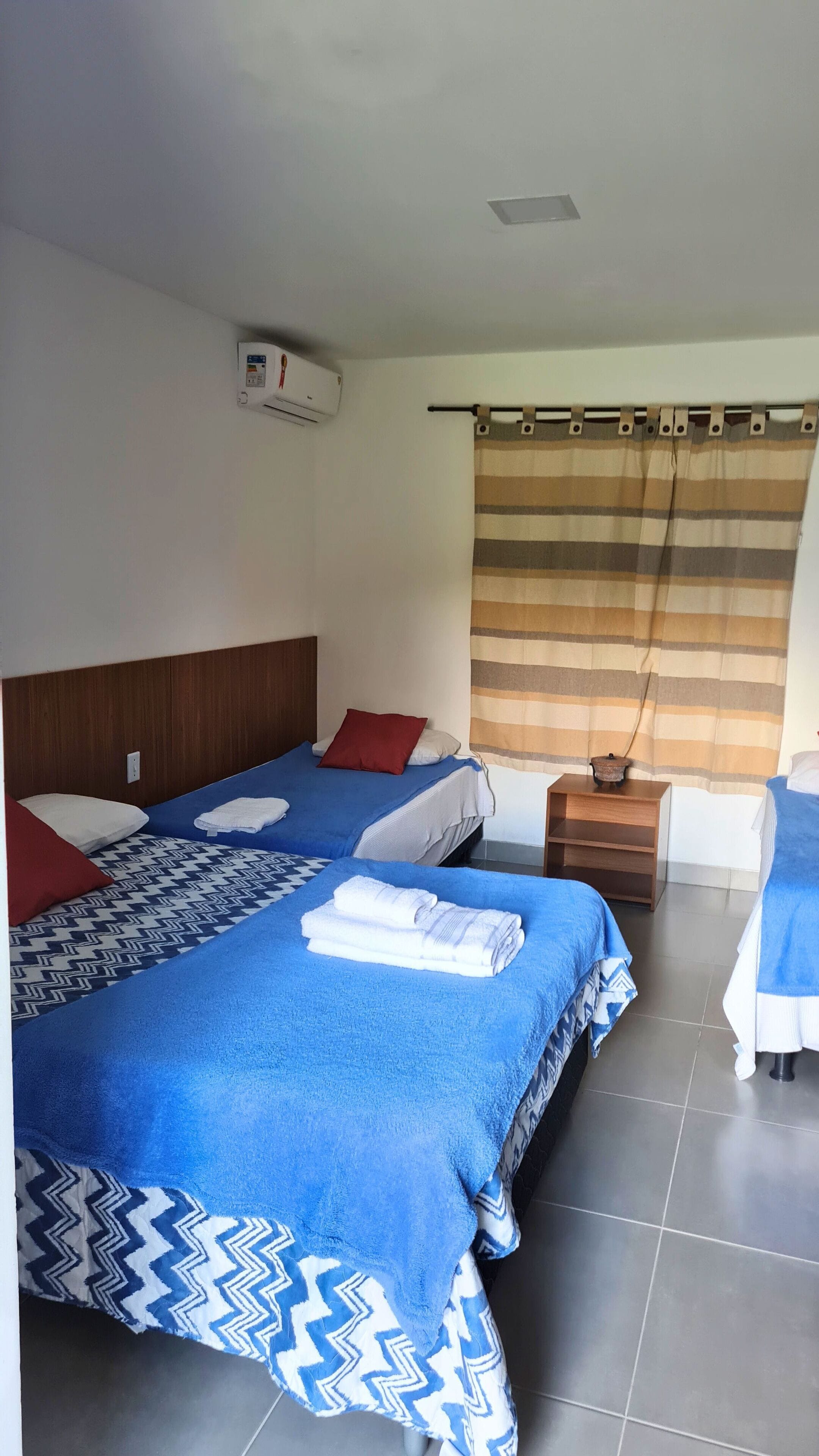 A hotel room with two beds, a wooden headboard, a striped curtain, and a small table with a lamp.