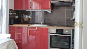 A compact kitchen with red cabinets, a built-in oven, and a microwave. - Comfortable 2-star studio near spa, pets allowed (Balaruc-les-Bains)