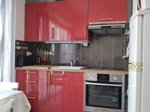 Kompakti keittiö, jossa on punaiset kaapit, sisäänrakennettu uuni ja mikroaaltouuni.