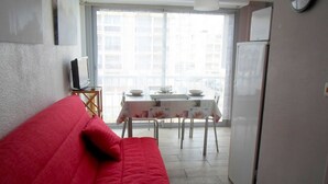 A compact living space with a red sofa, a dining table with chairs, a television, and a refrigerator. - Comfortable 2-star studio near spa, pets allowed (Balaruc-les-Bains)