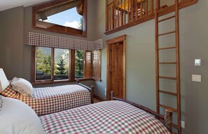 A bedroom with two beds, a window with a view of trees, a wooden ladder, and a door.