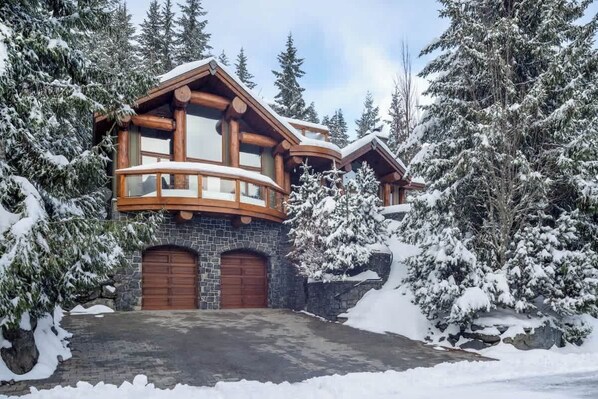 A log cabin with a stone foundation, wooden balconies, and a garage.
