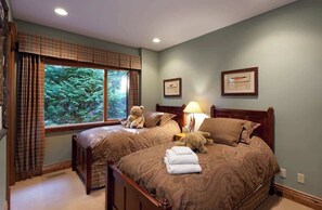 A bedroom with two beds, a window with curtains, a bedside lamp, and framed pictures on the wall. - Alpine chalet w/ hot tub & rooftop deck (Whistler)