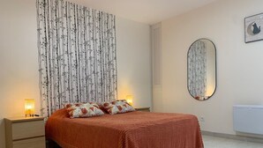 Ein Schlafzimmer mit einem Bett, zwei Nachttischen, einem Spiegel und einer Wand mit einem blumigen Vorhang.