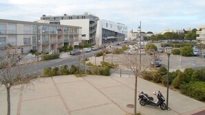 A modern building with a glass facade, a parking lot with several cars, and a scooter parked on the sidewalk.