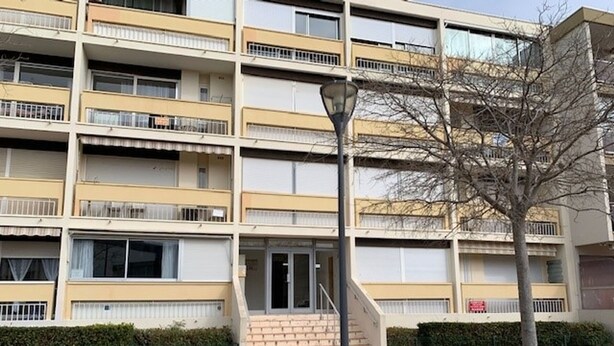 A multi-story apartment building with balconies, a central entrance with steps, and a street lamp.