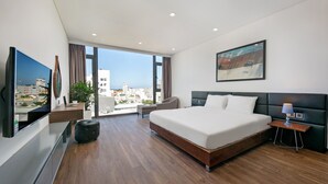 A modern hotel room with a large bed, a flat-screen TV, a desk, and a view of the city.