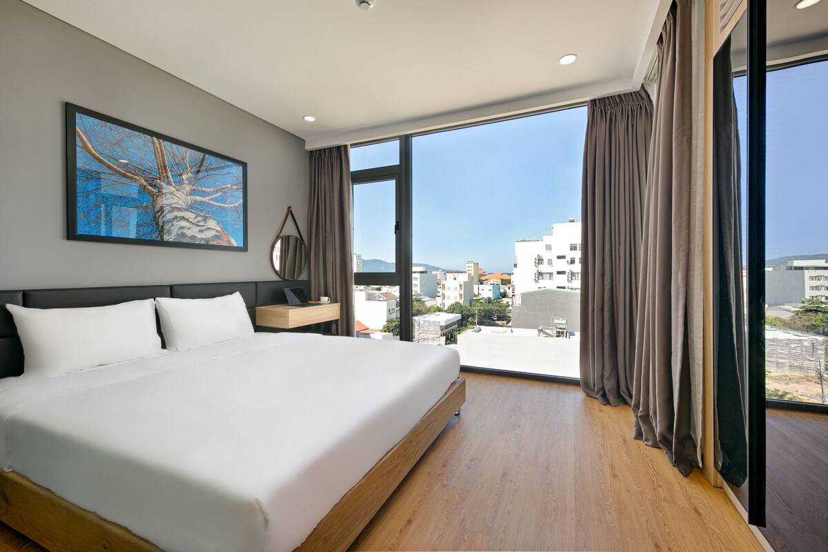 Ein modernes Hotelzimmer mit einem großen Bett, Blick auf die Stadt und einem Gemälde an der Wand.