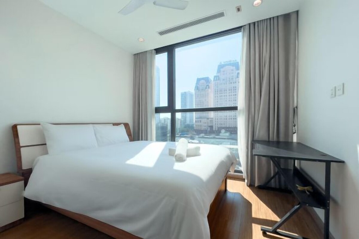 Habitación de hotel con cama, escritorio, ventana con cortinas y vista a la ciudad.