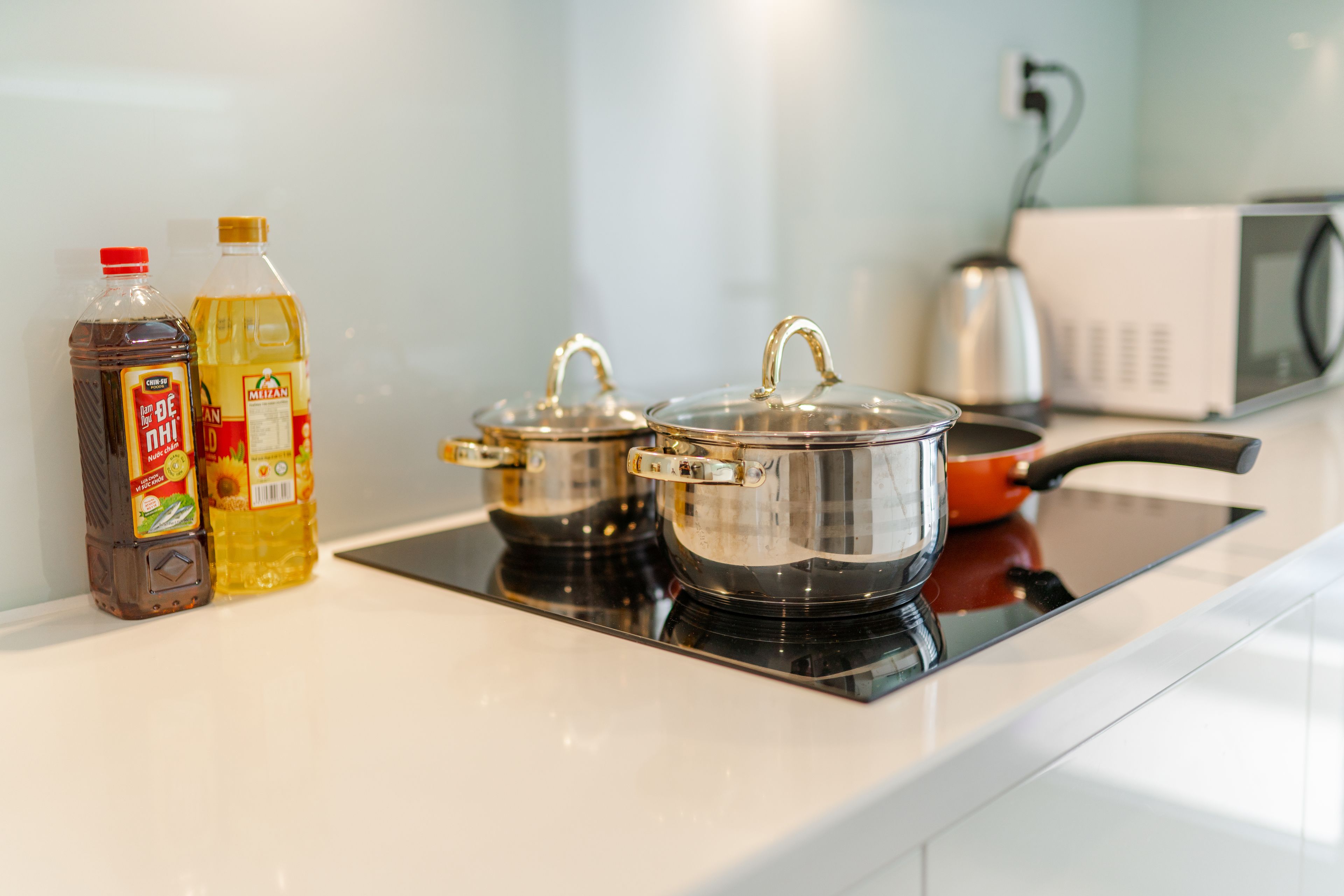 A kitchen with a microwave, a kettle, and two pots on an induction cooktop.
