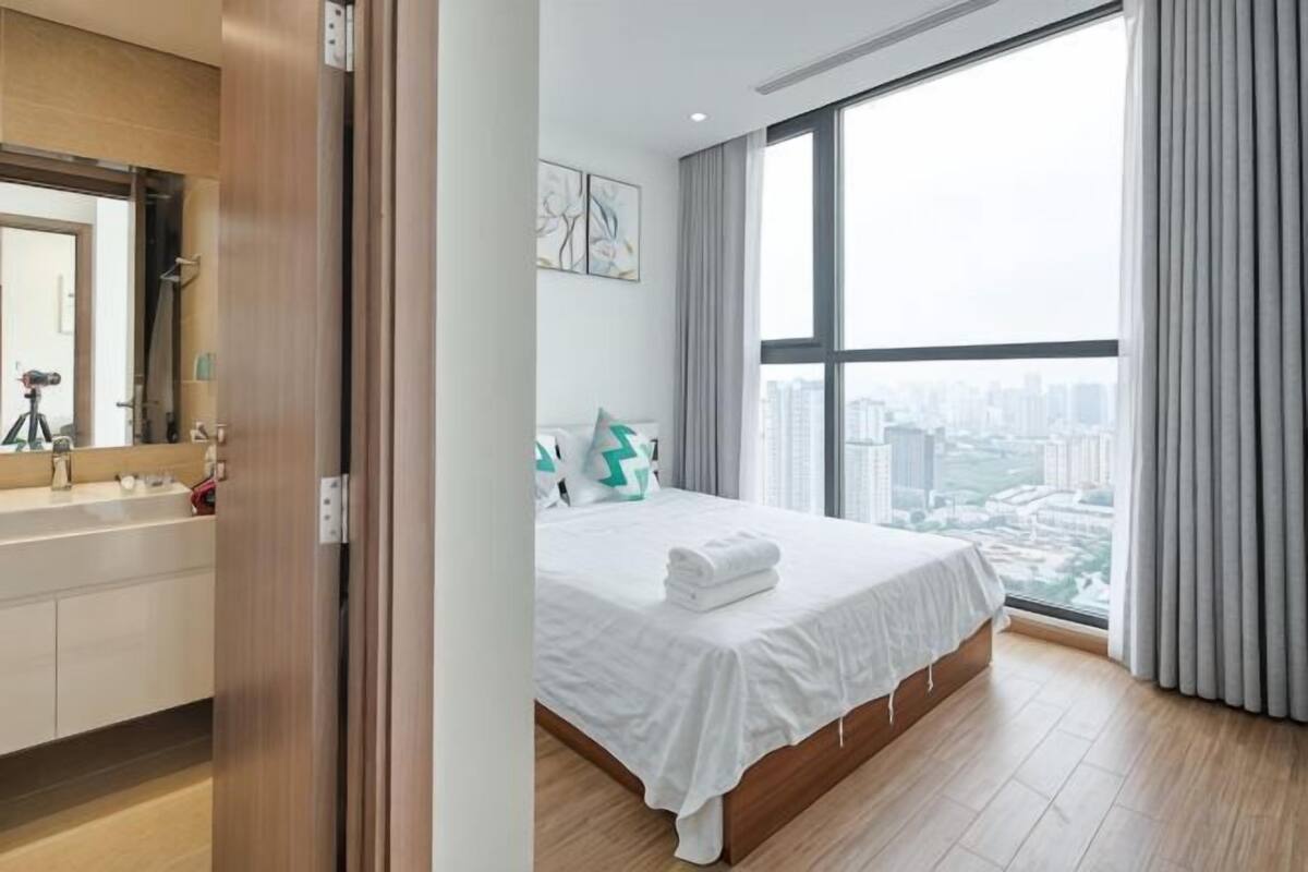 A bedroom with a large window, a bed, a bathroom with a mirror, and a city view.