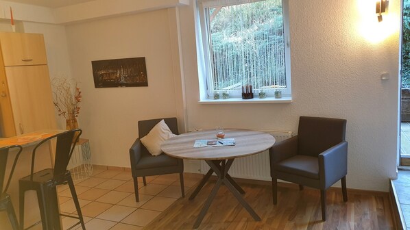 A dining area with a round table, two chairs, a vase with branches, and a framed picture on the wall. - At the gates of Hamburg, in the old country (Mittelnkirchen)