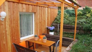 Puuinen terassi, jossa on pergola, pöytä tuoleineen ja penkki.