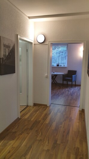 A hallway with wooden flooring, a round wall light, a window with a view of trees, and a chair in a corner. - At the gates of Hamburg, in the old country (Mittelnkirchen)