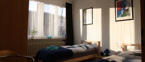 A bedroom with two single beds, a chair, and a radiator.