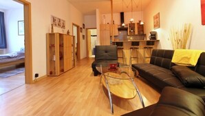 Een moderne woonkamer met een bank, een glazen salontafel en een eethoek met krukken. Achtergrond is een keuken.