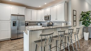 A modern kitchen with white cabinetry, stainless steel appliances, a granite countertop, and bar stools. - Luxury Home with PRIVATE POOL!  Pet Friendly and Wifi (North Myrtle Beach)