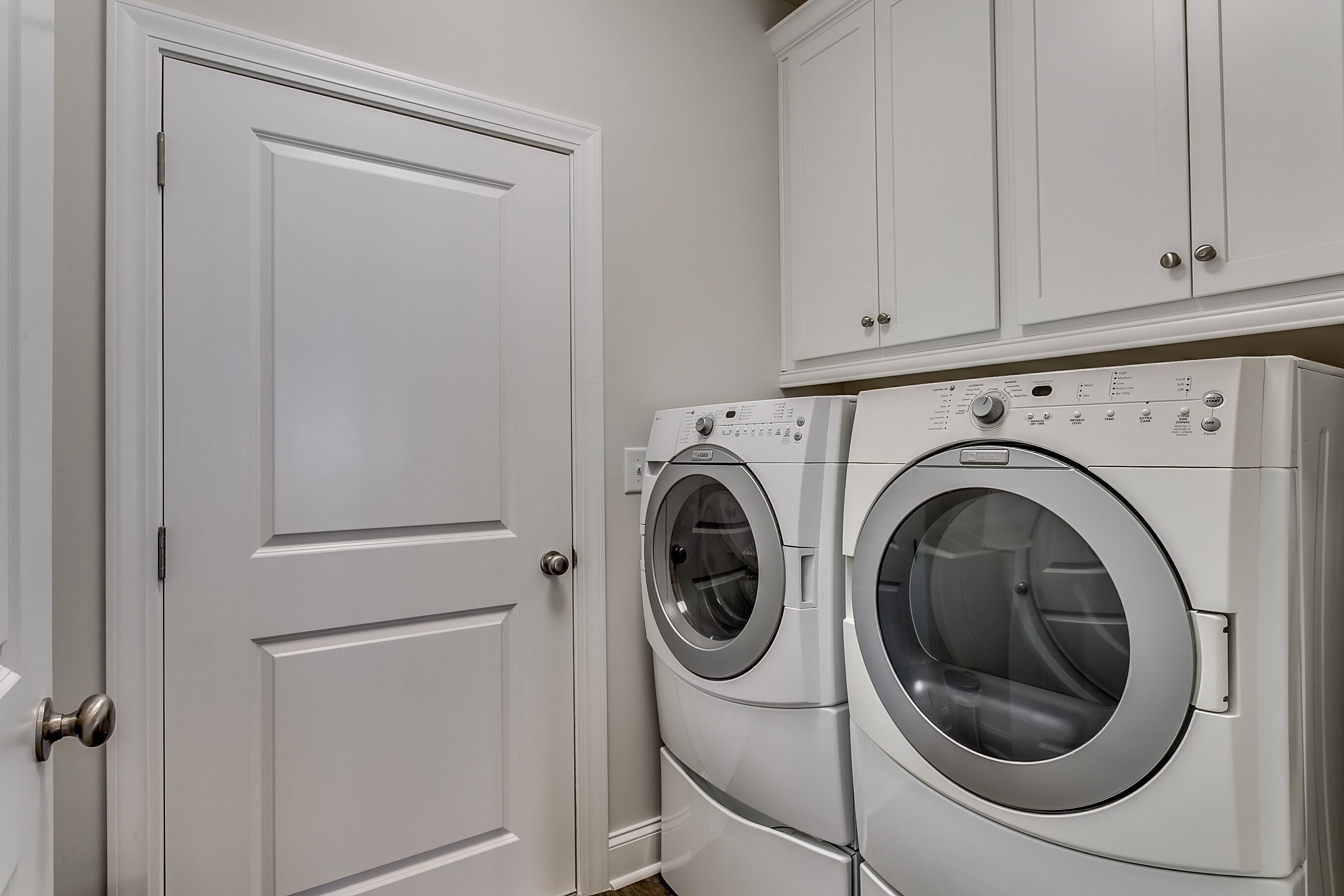 A laundry room with two front-loading washing machines and a white door.