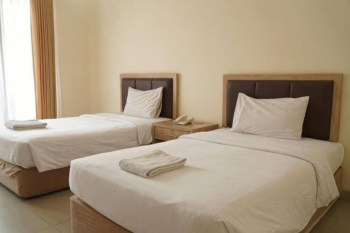 Two twin beds with white linens, wooden headboards, bedside tables with lamps, and a telephone.