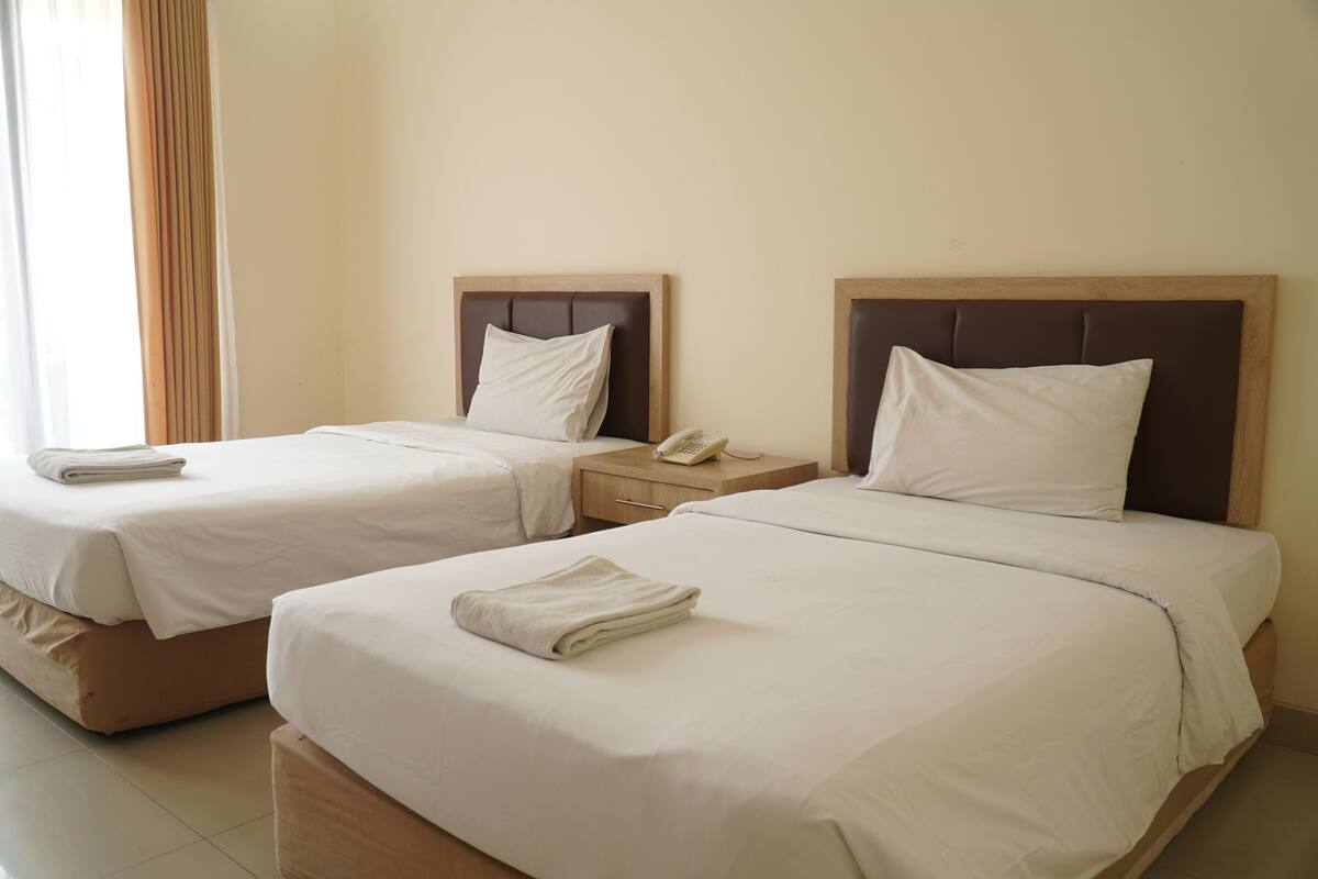 Two single beds with wooden headboards, white linens, and a bedside table with a telephone.