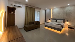 Una habitación de hotel moderna con una cama, un sofá, un escritorio de madera y un equipo de aire acondicionado.