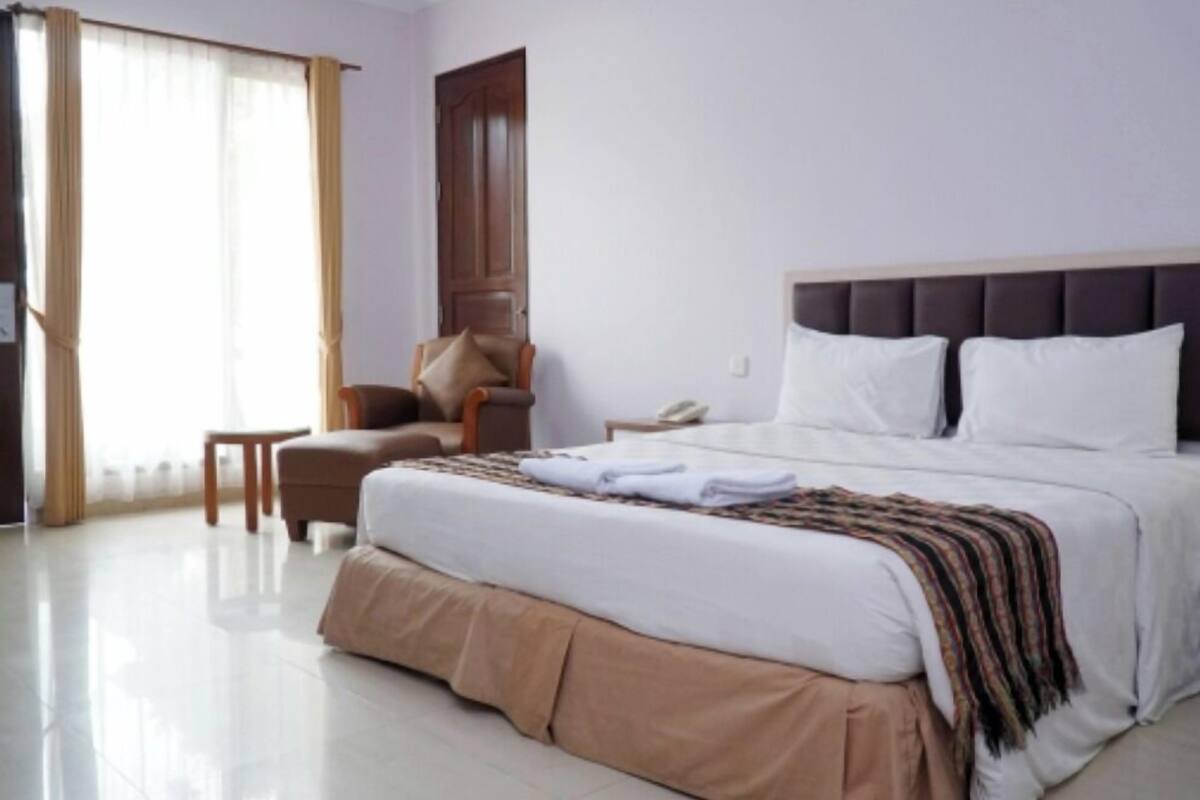 A hotel room with a large bed, a chair, a small table, and a door.