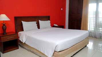 A neatly made bed with white linens in a room with red walls and a wooden headboard.