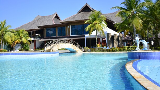 Un resort con una amplia piscina, palmeras y un edificio con techo de paja.