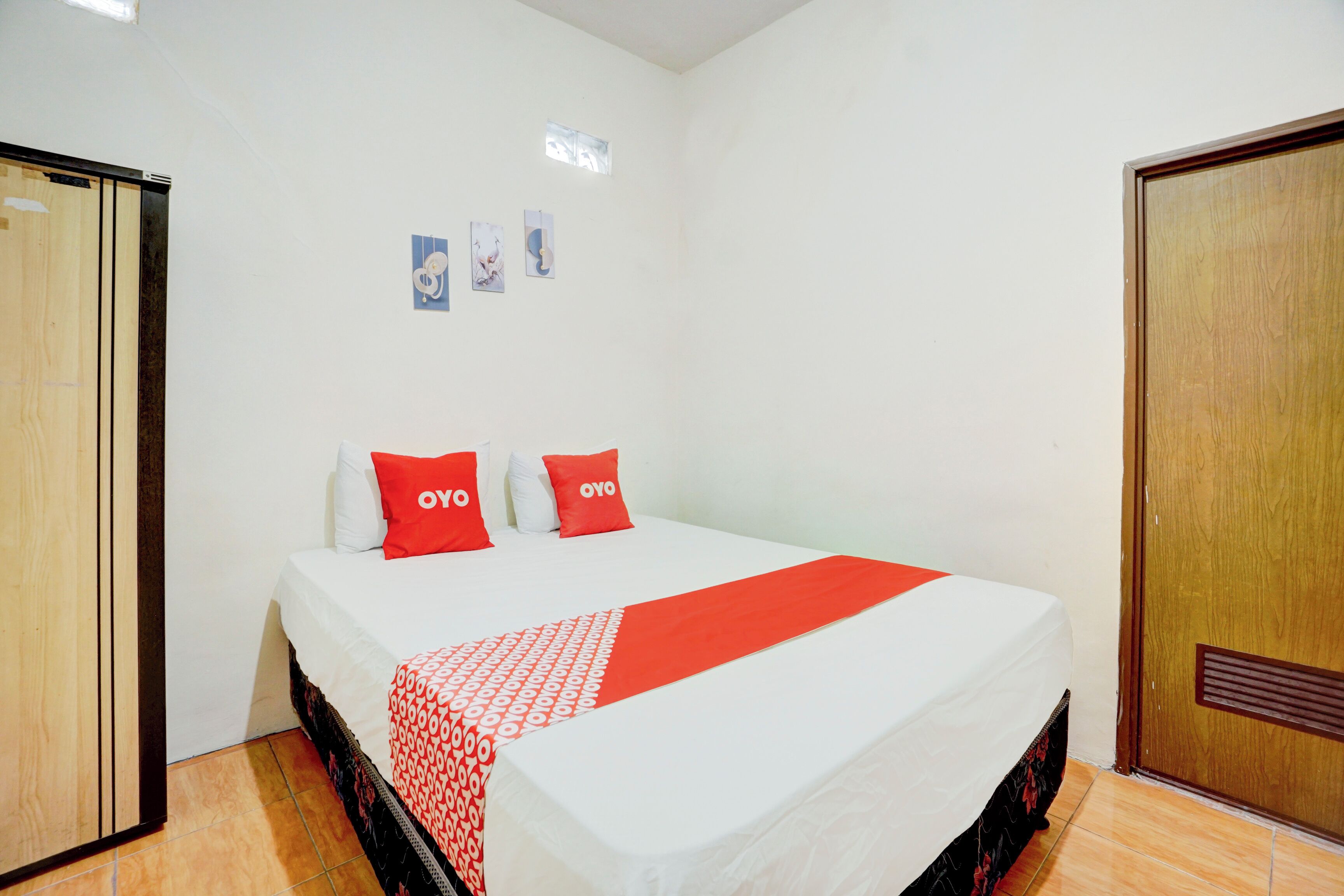Camera d'albergo con un letto, due cuscini rossi, una coperta bianca e una coperta decorata con un motivo rosso e bianco.