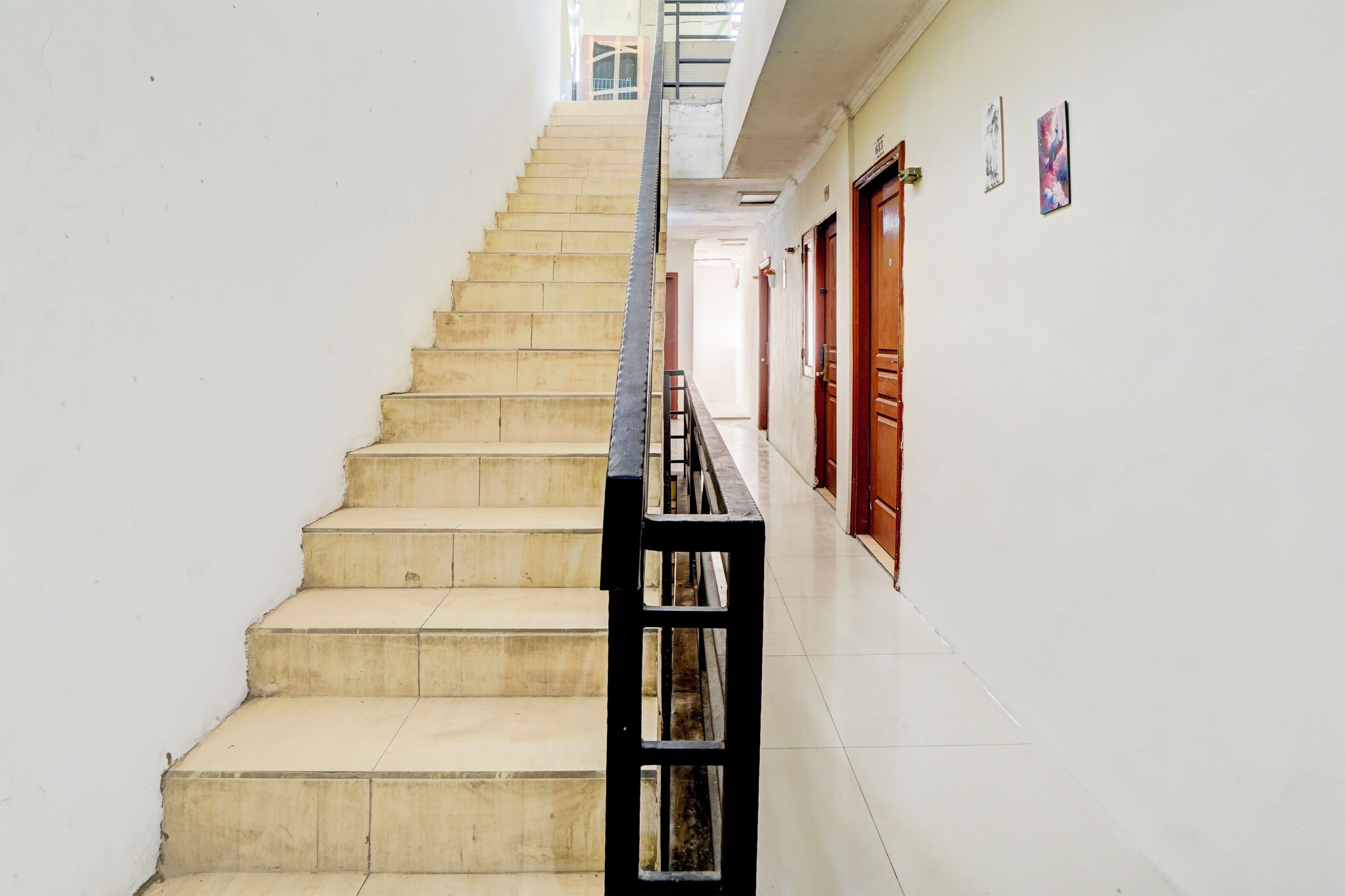A staircase with a black metal railing, leading to a landing with wooden doors and a white wall with framed artwork.