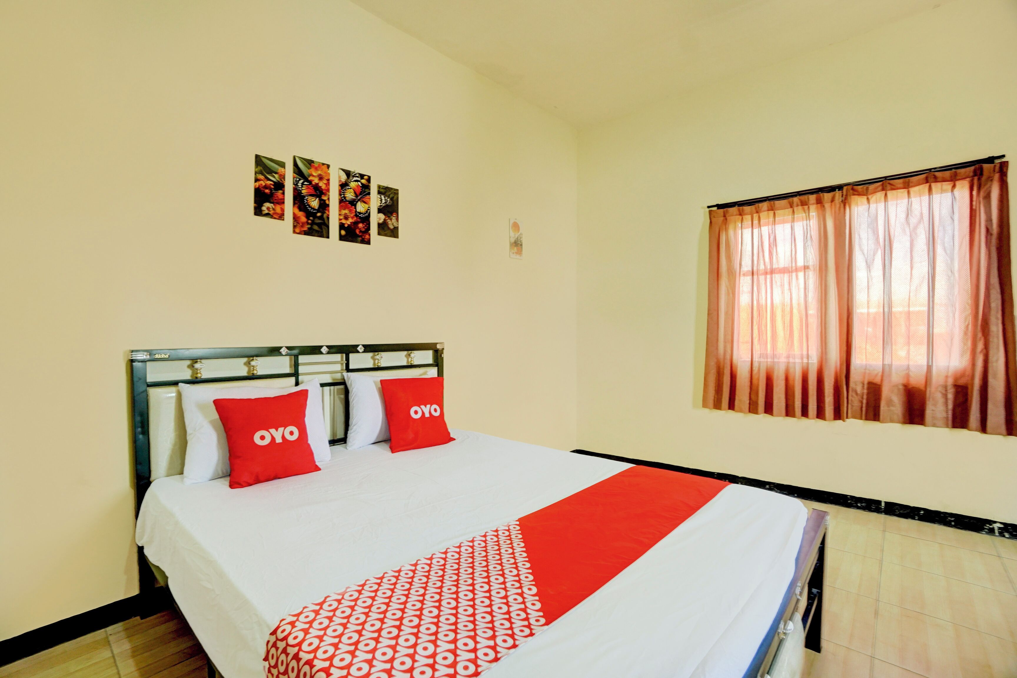 A hotel room with a bed, two red pillows with "OYO" branding, a patterned throw, and a window with curtains.