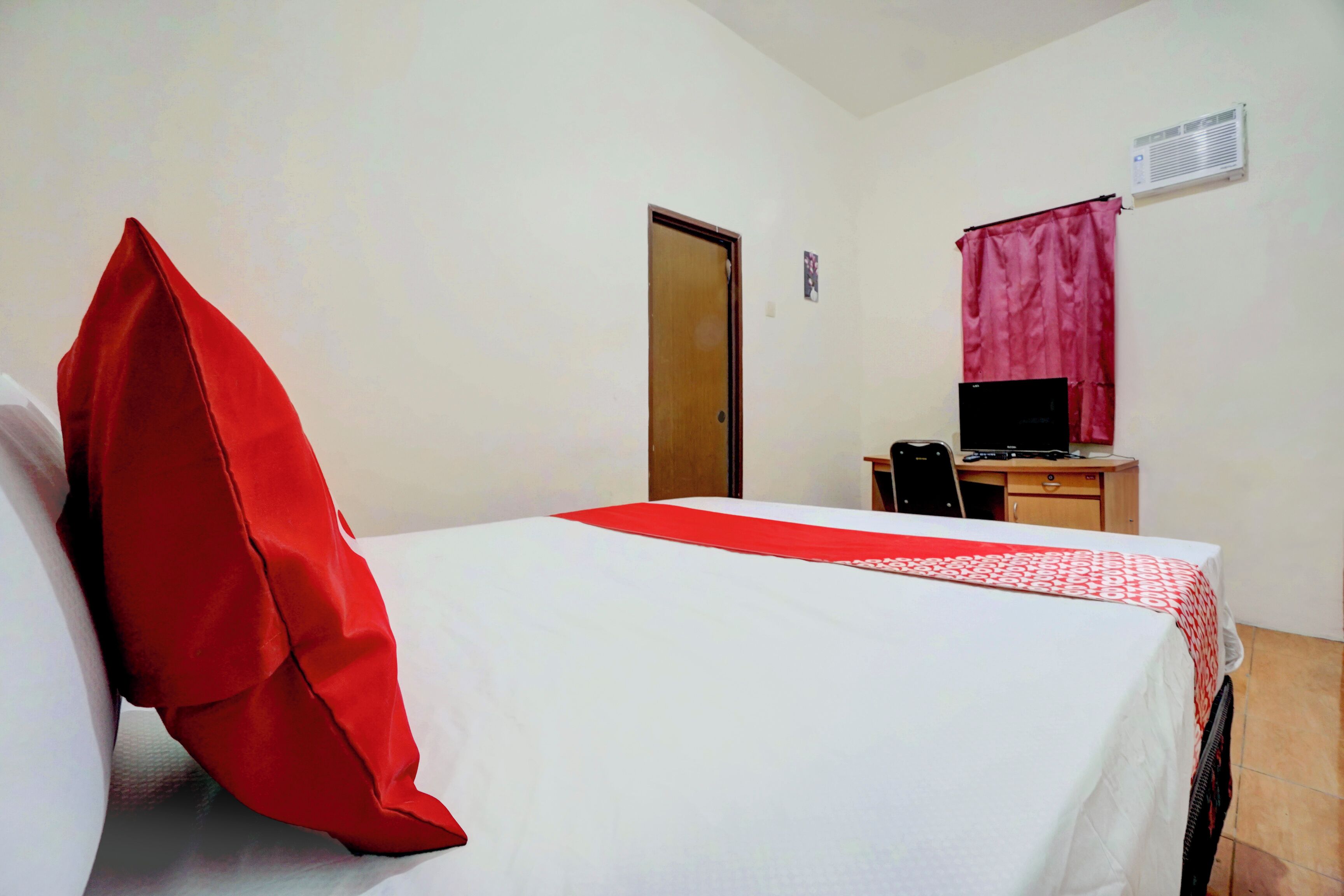 A hotel room with a bed, a desk, a chair, a computer, and a door.