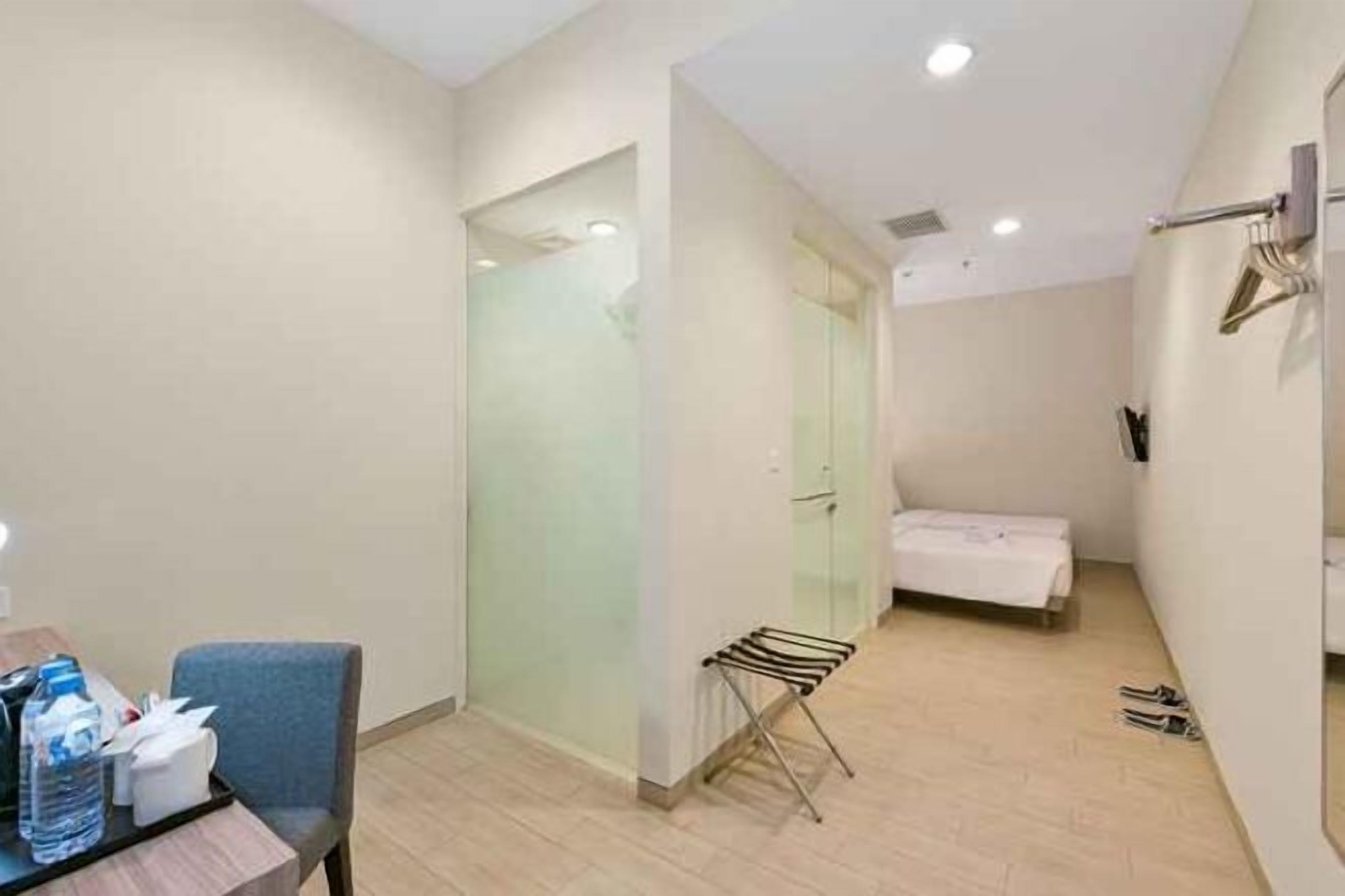 Habitación de hotel con cama, una mesita de noche con artículos de aseo, una silla, toallero y zona de ducha.