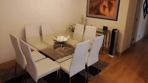 A dining area with a glass table and white chairs, a painting on the wall, and a radiator in the corner.