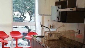 A modern kitchen with a gas stove, a microwave, and a sink. There are red chairs and a window with a view of trees and a car outside.